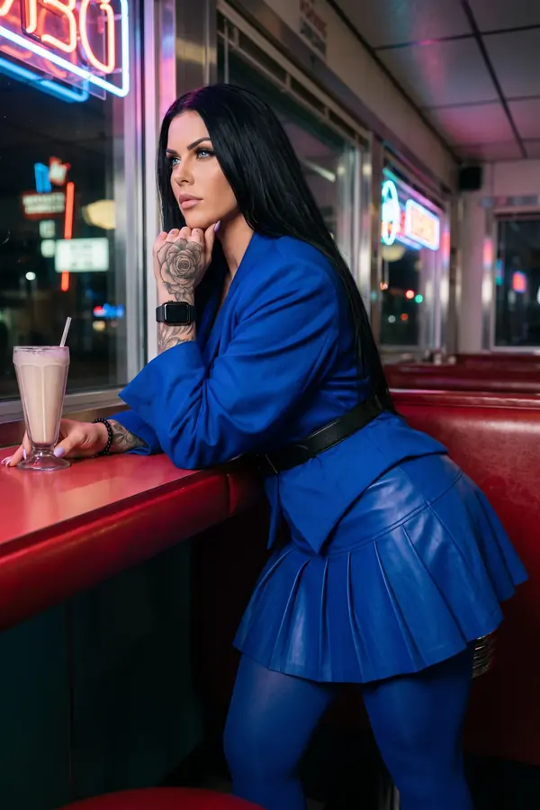 Woman in a belted cobalt wool blazer, pleated cobalt leather mini skirt and blue tights leaning on a diner counter