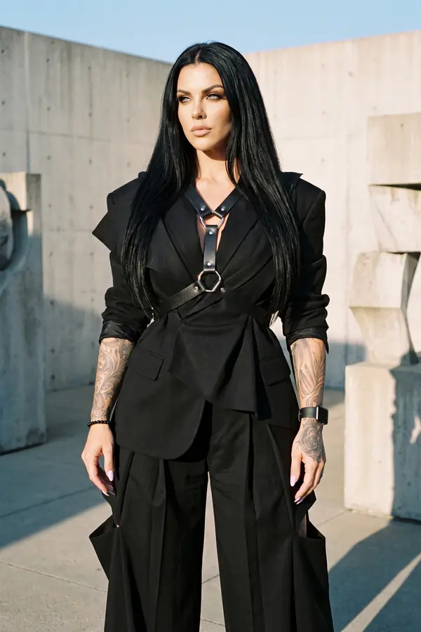 Woman in a black wool blazer with a leather O-ring strap belt and black pleated wide-leg trousers in a concrete sculpture garden