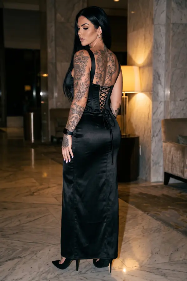 Woman seen from behind in a floor-length black satin gown with a laced open back and black pumps in a marble hotel lobby