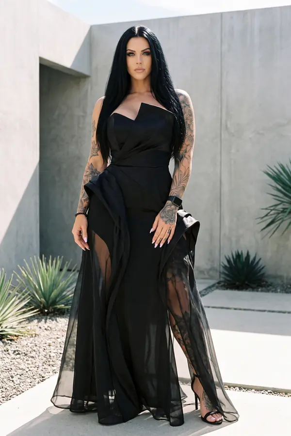 Woman in a black strapless satin gown with a hip peplum and organza overskirt in a concrete courtyard with agaves