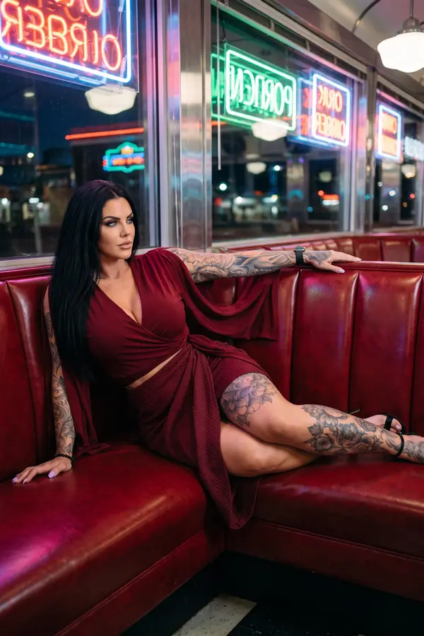 Woman seated in a red diner booth in a burgundy cape-sleeve wrap top, matching textured wrap skirt and black sandals
