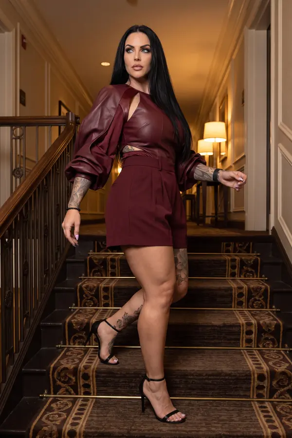 Woman in a burgundy faux leather balloon-sleeve top and burgundy tailored shorts walking down a carpeted hotel staircase