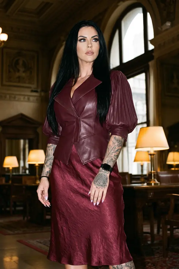 Woman in a burgundy leather puff-sleeve jacket and wine satin midi skirt in a wood-panelled reading room