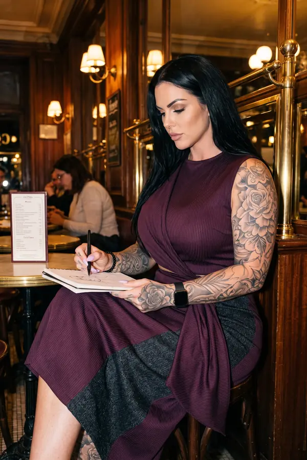 Woman seated in a brasserie sketching in a notebook, in a burgundy ribbed knit midi dress with charcoal panels