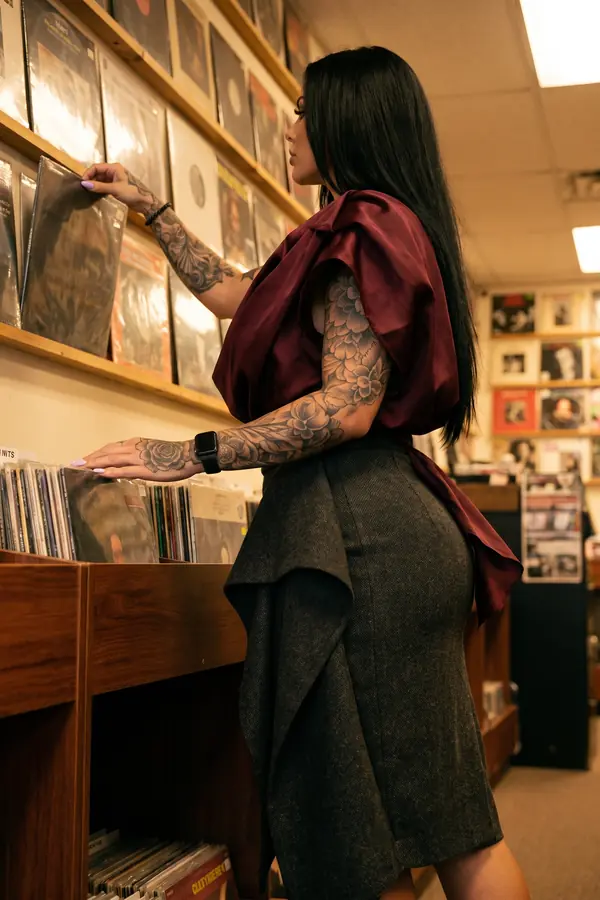 Woman in profile in a burgundy satin draped top and charcoal tweed pencil skirt browsing records in a shop