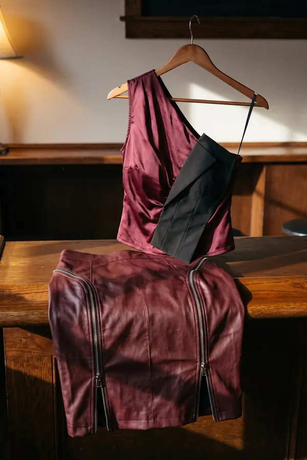 Woman in a burgundy satin one-shoulder top with a black panel and a burgundy leather zip pencil skirt in a wood-panelled bar