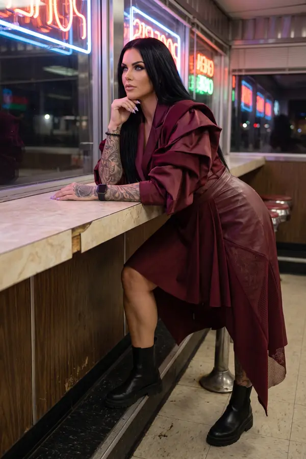 Woman in a burgundy satin ruffle blazer with a leather and mesh panel skirt and black chelsea boots at a diner counter