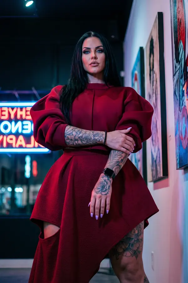 Woman in a burgundy puff-sleeve mock-neck top and matching asymmetric skirt with a hip cut-out in an art gallery