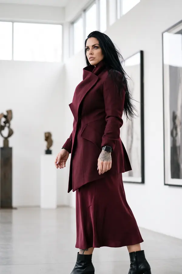 Woman in a fitted burgundy wool coat with a tall collar and burgundy satin midi skirt walking through a white art gallery