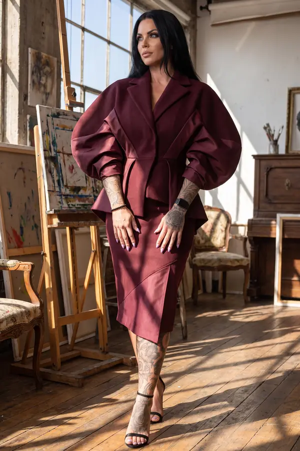 Woman in a burgundy wool jacket with huge satin-panelled balloon sleeves and a matching pencil skirt in a sunlit studio
