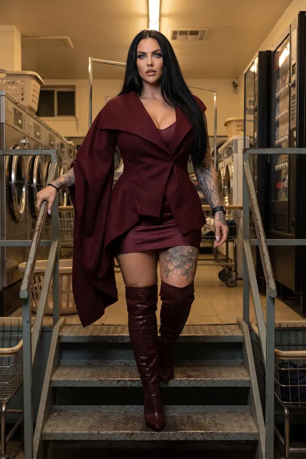 Woman in a burgundy draped wool jacket, satin mini skirt and croc over-the-knee boots walking down laundromat steps