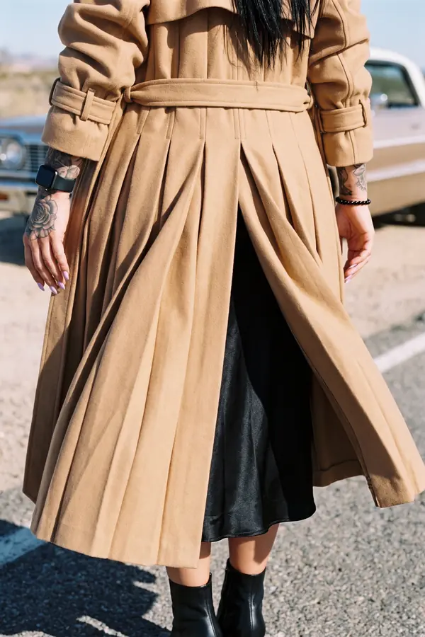 detail: Camel trench with a pleated back over a black slip dress