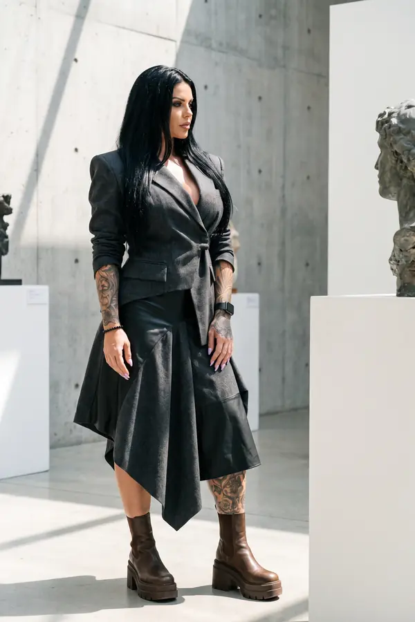 Woman in a charcoal wool blazer and wool and leather handkerchief skirt with brown platform boots in a concrete gallery
