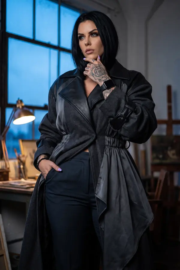 Woman in an oversized charcoal wool coat with leather lapels and grey satin drape over navy trousers, studio at dusk