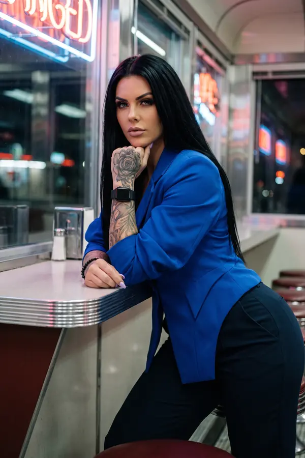 Woman in a fitted cobalt crepe blazer and high-waisted navy trousers leaning on a chrome diner counter at night