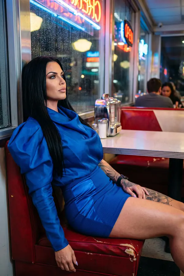 Woman seated in a diner booth by a rainy window in a cobalt organza puff-sleeve top and cobalt mini skirt with satin panel