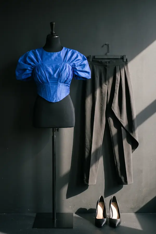 Woman in a cobalt taffeta corset top with puff sleeves and black pleated tapered trousers on a neon-lit street at night
