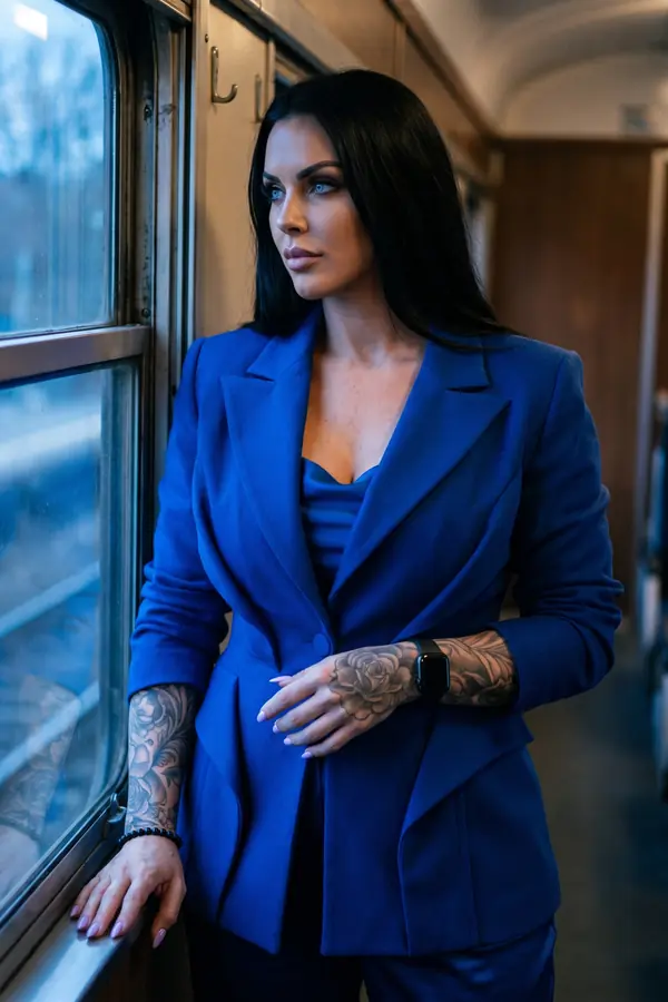 Woman in a cobalt wool blazer over a satin cowl-neck camisole looking out of a train corridor window