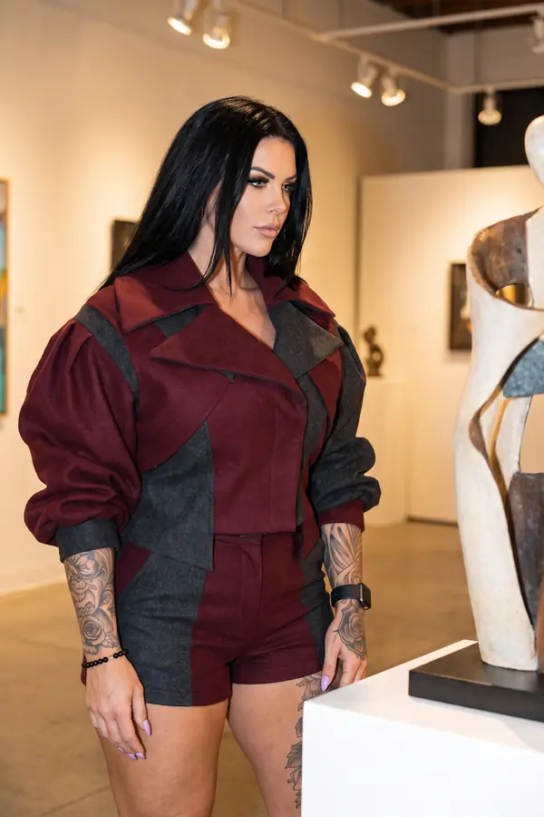 Woman in a cropped burgundy and charcoal colour-block wool jacket and matching shorts looking at a sculpture in a gallery