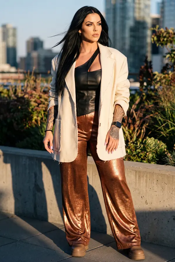 Woman in copper metallic wide-leg trousers, a black leather corset top and an oversized ivory blazer on a rooftop garden