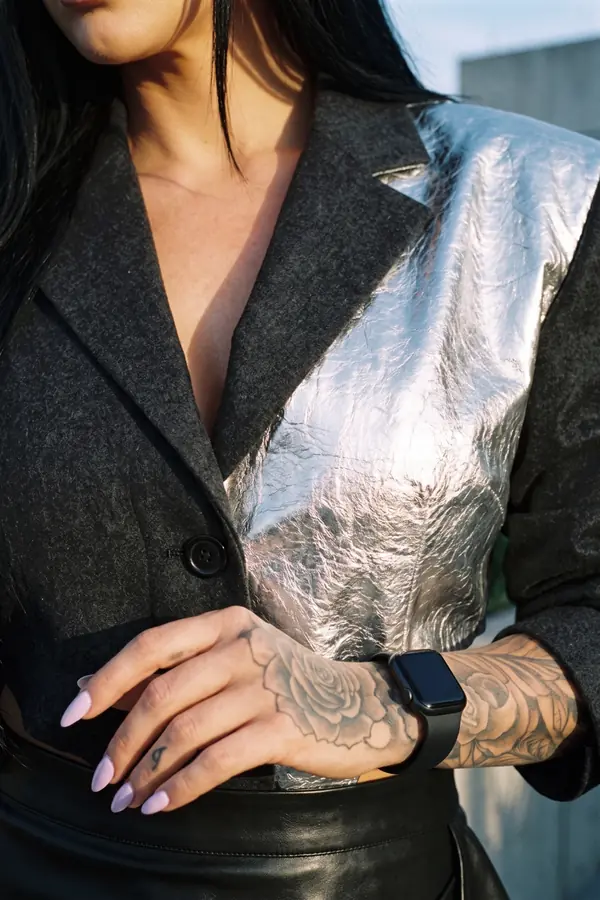 Woman in a cropped charcoal wool blazer with a silver leather panel and a black leather draped skirt on a terrace