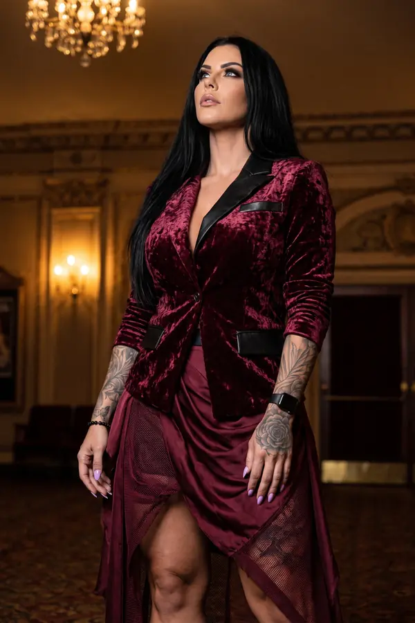 Woman in a burgundy crushed velvet blazer with leather lapels and an asymmetric satin and mesh skirt in a grand lobby