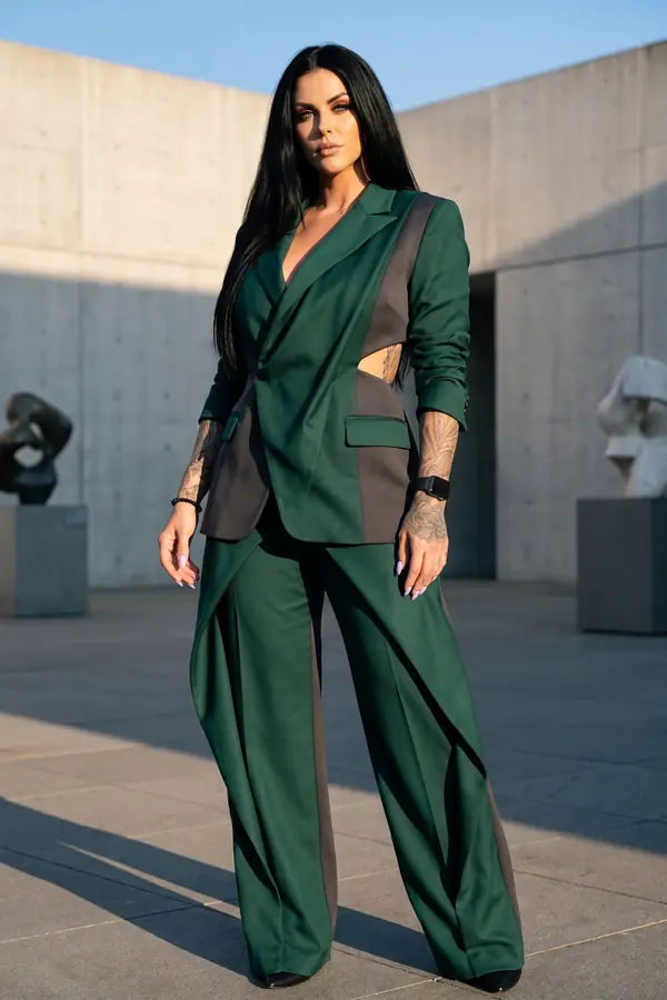 Woman in an emerald wool suit with charcoal side panels and waist cut-outs in a concrete sculpture plaza at sunset
