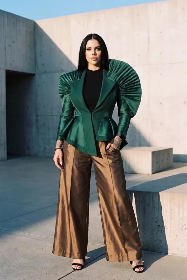 Woman in an emerald satin blazer with pleated fan shoulders, black leather bandeau top and bronze wide-leg trousers