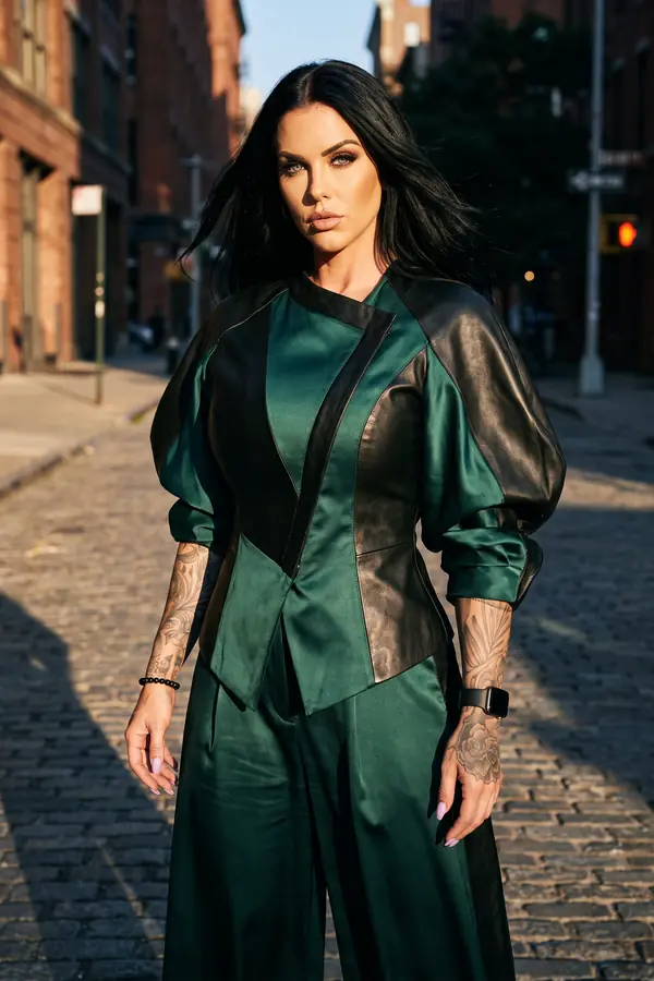 Woman in an emerald satin and black leather panelled jacket with matching wide-leg trousers on a cobbled city street