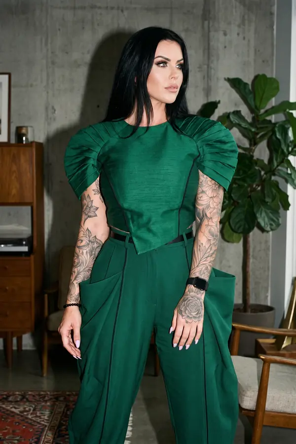 Woman in an emerald shantung top with fanned pleated sleeves and matching draped trousers in a mid-century living room