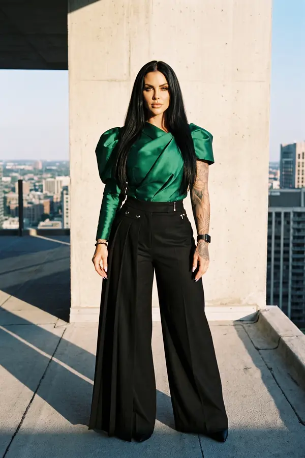 Woman in an emerald silk shantung top with puff shoulders and black pleated wide-leg trousers on a concrete rooftop