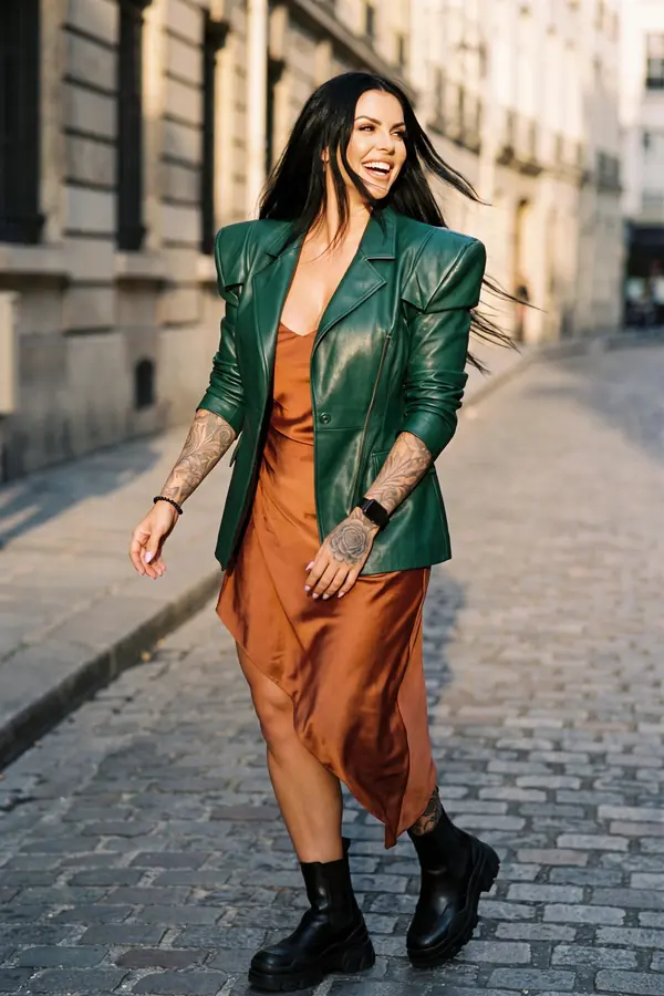 Woman walking on a cobbled street in a forest green leather blazer over a rust satin slip dress and chunky black boots