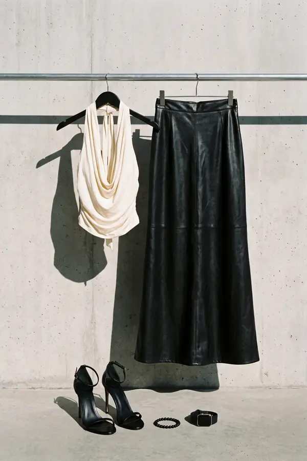 Woman in an ivory cowl-neck halter top and black leather maxi skirt with a side slit seated on a lit marble staircase