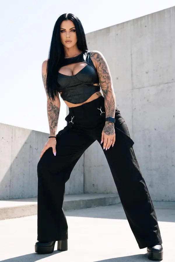 Woman in a black leather cut-out bustier, black wide-leg trousers with clip straps and platform boots on a concrete roof