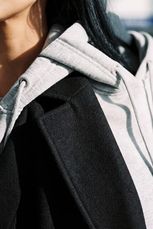 detail: Long black wool coat over a grey hoodie and straight jeans