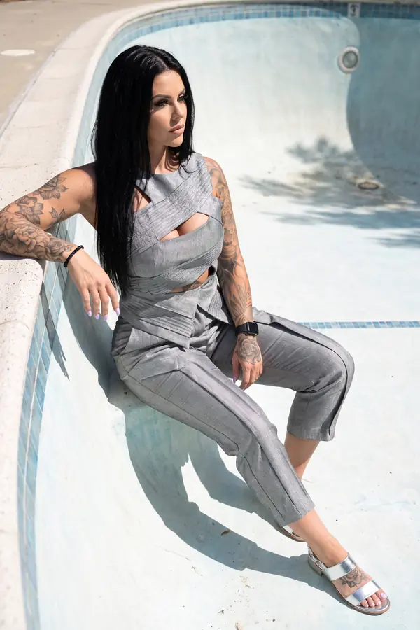 Woman in a grey metallic linen crossover top and cropped trousers sitting on the sloped wall of an empty swimming pool