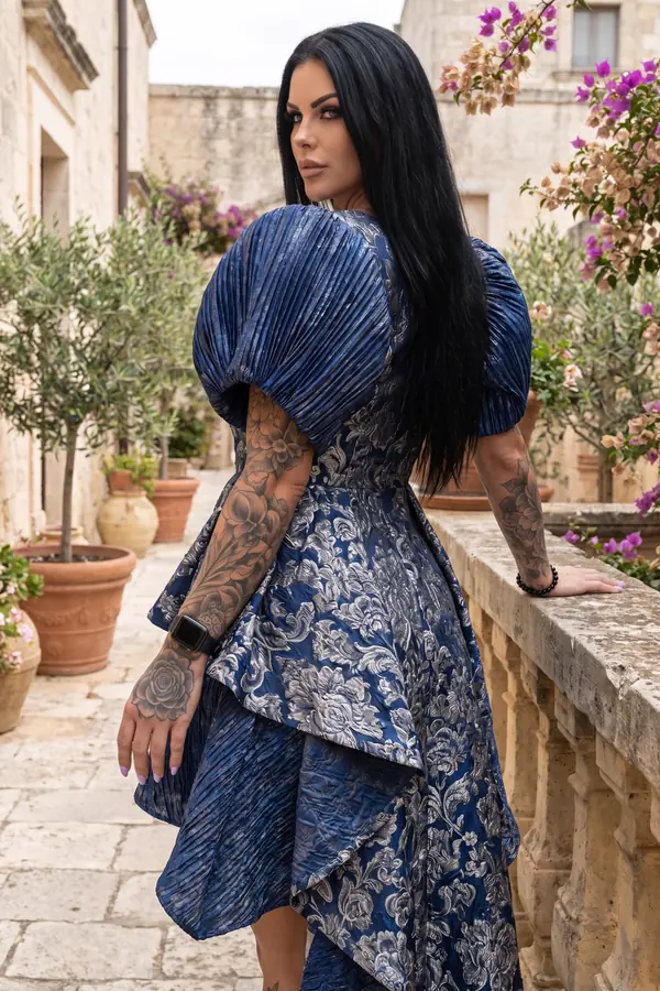 Woman seen from behind in a navy and silver brocade dress with pleated metallic puff sleeves on an old stone street