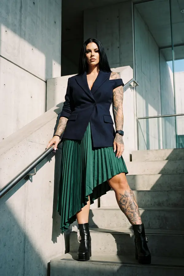 Woman in a navy cut-out shoulder blazer, emerald pleated skirt and black platform boots on concrete stairs