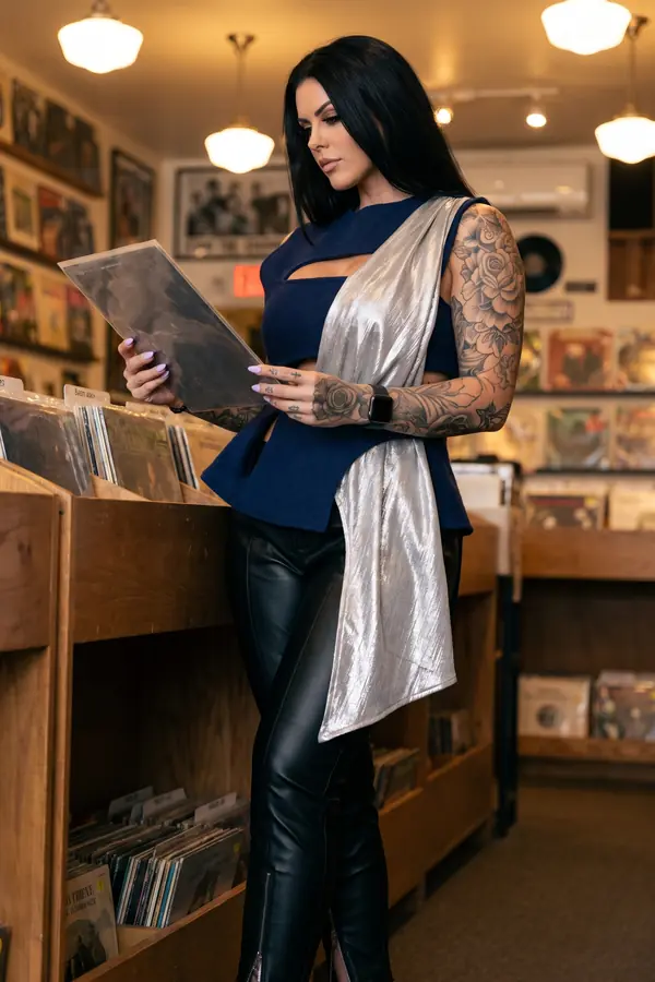 Woman in a sleeveless navy wool peplum top with a silver lamé sash and black leather trousers browsing records in a shop