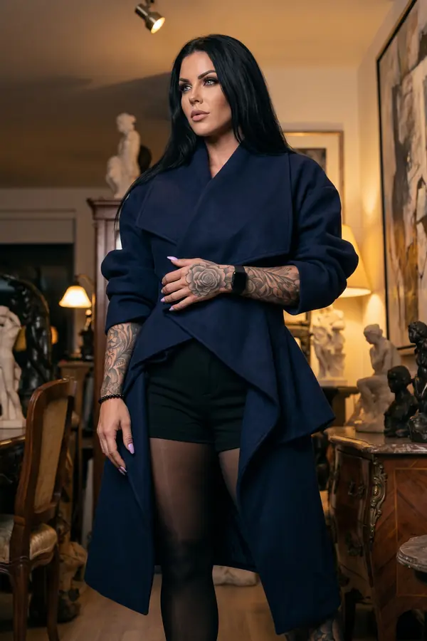 Woman in an oversized navy wool waterfall coat over black tailored shorts and black tights in an antiques shop