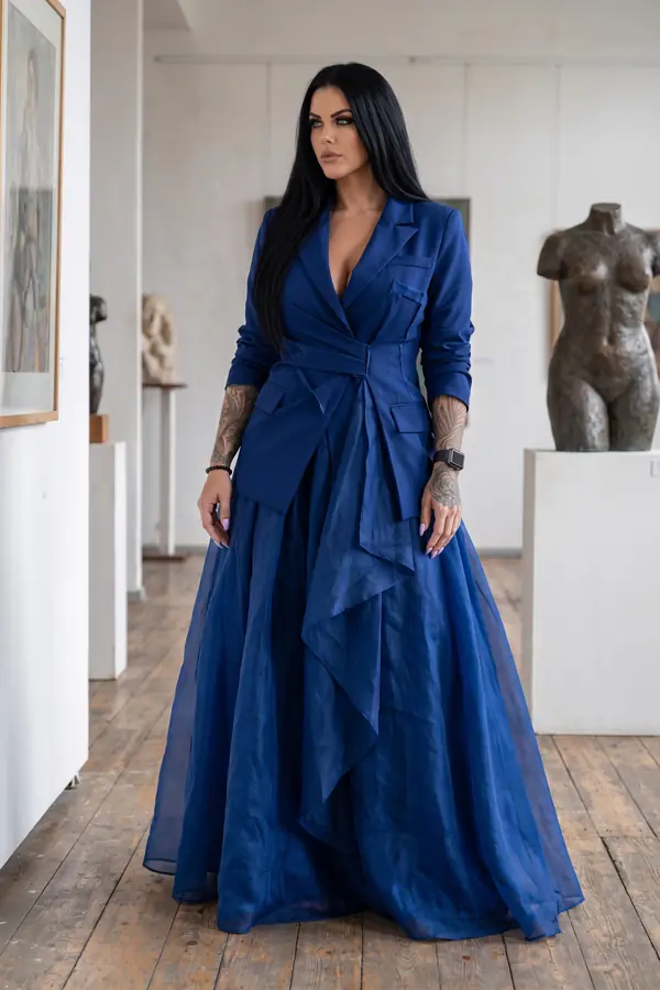 Woman in a navy wrap blazer and floor-length navy organza skirt standing in a gallery with bronze sculptures