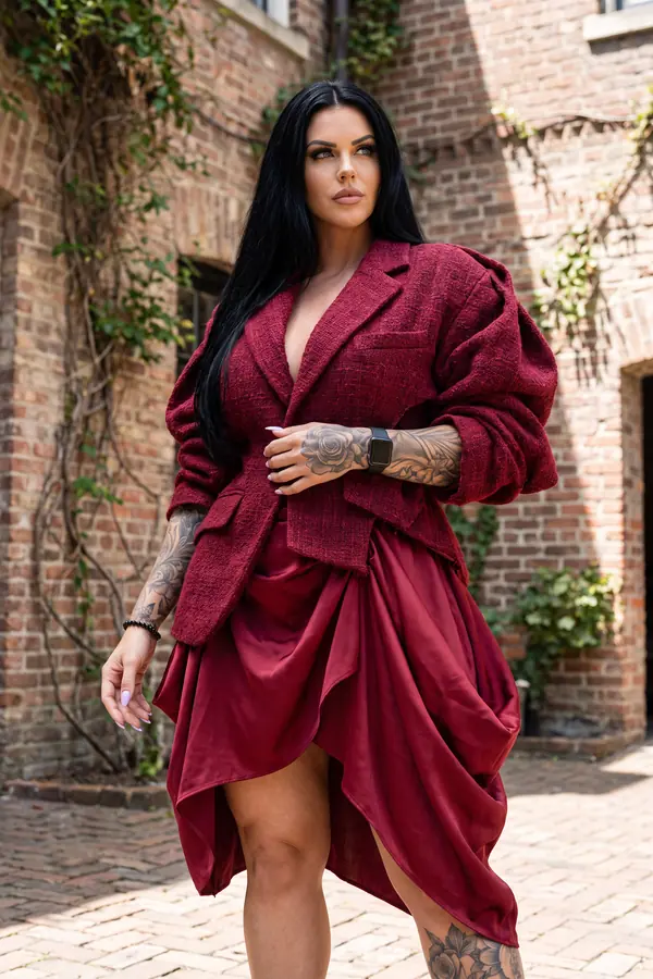 Woman in an oversized burgundy boucle tweed blazer and a draped red satin bubble-hem skirt in a brick courtyard