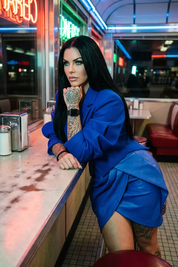Woman in an oversized cobalt wool blazer and cobalt leather wrap mini skirt leaning on a diner counter at night