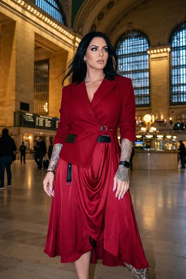 Woman in a red wool wrap blazer with black leather trim and a red draped satin wrap skirt in a grand station hall