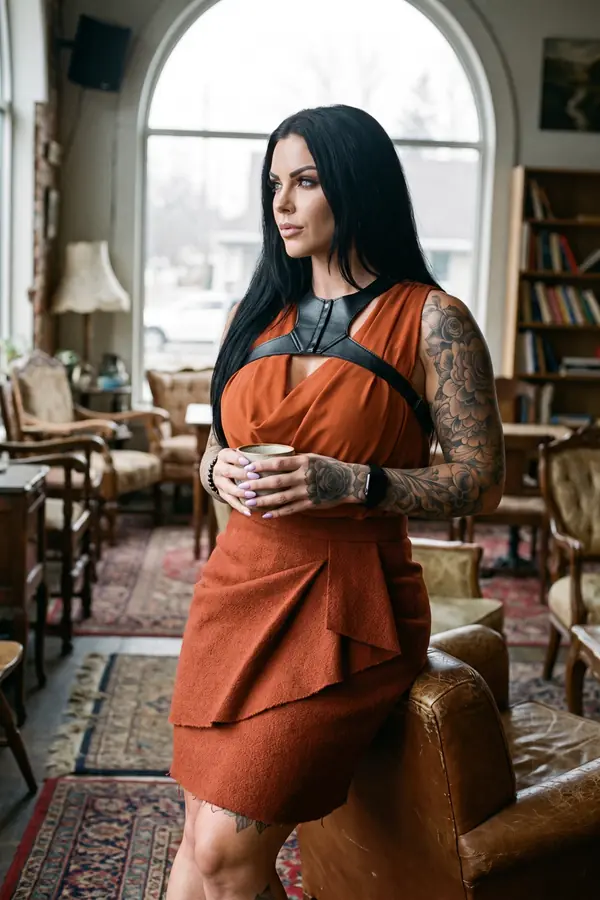 Woman in a rust draped top with black leather shoulder straps and a rust wool wrap skirt in a bookshop cafe
