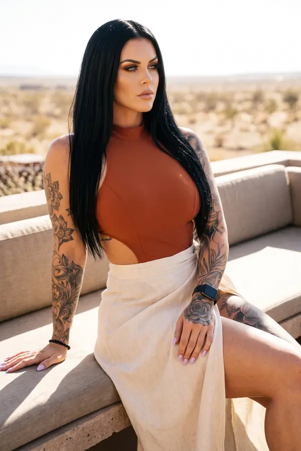 Woman in a rust halter bodysuit and a natural linen wrap skirt with a high side slit seated on a bench in the desert