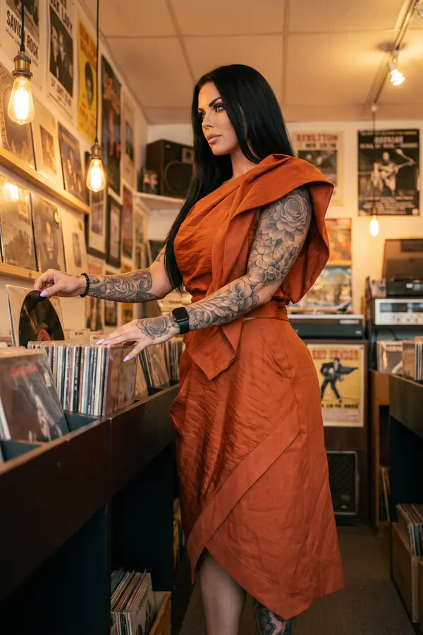 Woman in a rust linen draped top with a shoulder sash and a matching wrap midi skirt, browsing records in a shop
