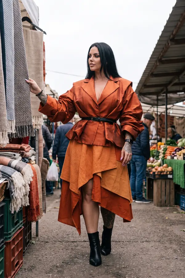 Woman in a rust taffeta belted jacket and layered ochre gauze skirt with black ankle boots at an outdoor market