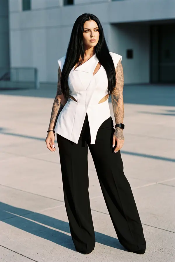 Woman in a white sleeveless sculpted vest top with cut-outs and black wide-leg trousers in a pale concrete plaza
