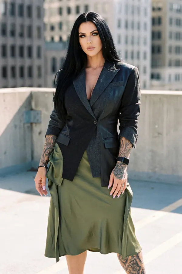 Woman in a charcoal wool and black leather patchwork blazer and an olive satin midi skirt on a car park rooftop